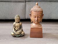 Photo showing both Buddha statues side by side on a floor in front of a gray sofa, depicting the size and general condition of the statues.