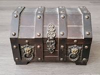 Front view of the wooden pirate chest shaped jewelry box showing the detailed metal straps, rivets, and lion head metal accents on the front.