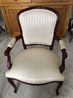 Front view of one of the two wooden armchairs with cream striped upholstery and carved detailing on the frame and arms.