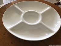Oval white ceramic serving tray with four compartments, displayed on a wooden surface.