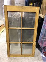 Wooden window frame in natural wood finish with six glass panes, showing visible signs of wear and age.