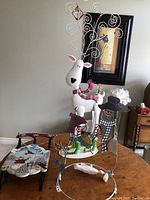 Three Christmas themed holiday decorations on a table against a wall. Includes a tall white reindeer with curled wire antlers, a snowman figure, and a winter child figure.