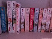 Photo showing two rows of Debbie Macomber paperback novels arranged vertically on two book shelves.
