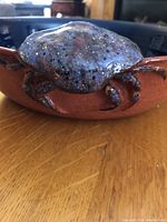 Close-up of crab figurine decoration on brown exterior of pottery bowl.