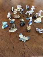 Group of small ceramic animal figurines on wooden surface, including owl, birds, butterfly, rabbit, and others.