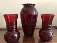 Front view of three ruby red glass vases with one tall etched floral vase and two smaller ribbed vases