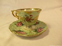 Castle China porcelain cup and saucer set showing floral design and gold trimmed edges, with ornate gold handle on cup.