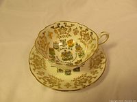 Photo of the teacup and saucer from an angle showing the Canada Coat of Arms design inside the teacup and gold decorative patterns on both pieces.