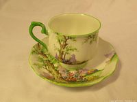 Royal Albert teacup and saucer showing detailed painted nature scene with flowers and trees, green handle and rim