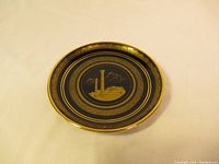 Top view of the decorative dish showing gold inlaid Greek column design on black background with gold trim around the edge.