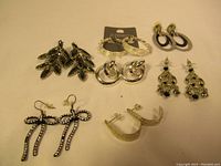 Top view showing eight pairs of earrings with various designs including leaf clusters, hoops, and ornate drops
