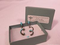 Pair of Lone Mountain Turquoise earrings in a Lone Mountain Turquoise Co. box. One turquoise piece is detached.