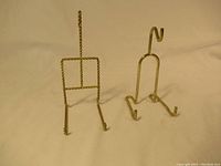 Photo showing two metal necklace jewelry stands, one twisted metal design and one smooth metal design, both gold-tone and slightly used.