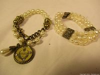Photo showing two vintage pearl bracelets on light background, one with three strands of faux pearls and decorative metal accents, the other with chains and charms including faux pearls.