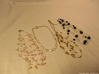 Four vintage necklaces displayed on a beige surface, showing different bead styles and colors; photo taken for full lot overview.
