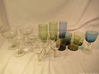 Front view showing full set of colored glasses, including green tall glasses, blue glasses, and clear stemware of coupe and wine shape.