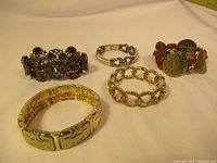 Five vintage bracelets shown together on beige background including various metal and beaded designs.