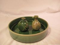 Two small decorative ceramic vases on a round green ceramic dish
