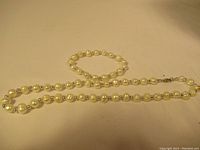 Pearl necklace and matching bracelet laid flat on beige background showing bead details and clasp.