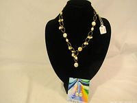 Pearl necklace displayed on black jewelry bust showing linked gold-tone chain and round white pearls.