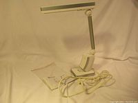 Vintage OttLite desk lamp displayed on a neutral backdrop with power cord coiled in front and plastic-bagged instruction manual beside it.