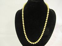 Full view of the pearl necklace displayed on black mannequin bust, showing the uniform round cream-colored pearls and classic length.