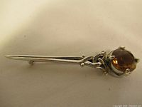 Top view of the vintage kilt pin showing the full length and ornate metalwork with amber-colored stone