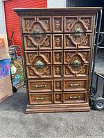 Front view of a wooden dresser with ornate carved drawer fronts and decorative knobs, showcasing traditional style and medium brown wood finish.