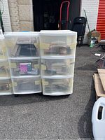 Six white plastic rolling drawer storage units with tapes, records, and CDs inside. Drawers are semi-transparent and taped shut in several units.
