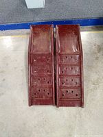 Top view showing two red metal ramps with numerous holes on the surface for traction.