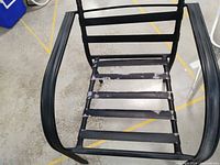 Close-up of one black metal frame camping chair showing wear on the seat slats without cushions.