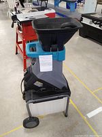 Front side view of an electric wood chipper shredder showing feeding chute, wheels, and collection bin.