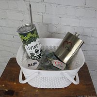 Gift basket items displayed without wrapping, showing a 20 oz camo thermal tumbler with straw, 8 oz stainless steel flask with Dad design, camo gaiter, aluminum keychain, and magnet in a white basket.