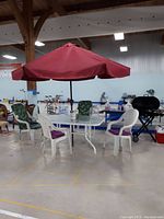 Front view of outdoor dining set showing table, four chairs, red umbrella, plastic jug on table in large indoor space
