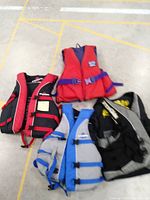 Lot includes four life jackets arranged on floor - various colors and brands visible