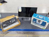 Memorex iMove boombox in original box next to HP 27-inch monitor and Logitech keyboard in box on floor surface.