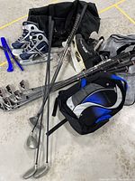 Full assortment of hockey skates, golf clubs, golf bags, and backpack on concrete floor