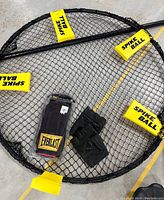 Spike Ball net with yellow tags, black leather boxing gloves on netted floor, new Everlast leather bag gloves in packaging.