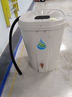 Photo of a beige plastic rain barrel with a lid featuring a screen, blue and green water droplet logo, and spigot near the bottom. A black hose is shown attached alongside the barrel.