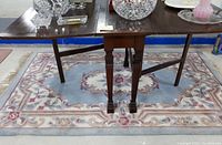 View of antique wooden Fife table standing on a pink and blue floral patterned area rug, showing table legs and rug design.