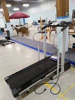 Photo of treadmill seen from side showing running belt, handrails, and frame. Accessories kit placed on running belt.