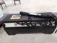 Side angle of black truck tool box with metal lock panel, windshield cover bag, strap, and calendar on top.