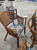 Single wicker armchair with cane back and blue floral cushion next to glass table edge