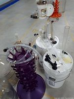 Wide view of wine making accessories arranged on floor showing carboys, buckets with equipment, purple drying racks, thermometers and small items.
