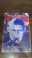 Front view of Hellraiser III Hell on Earth movie poster; shows detailed artwork of Pinhead and cityscape background, with visible wear and edge damage.