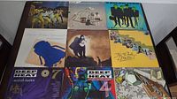 Photo showing 9 vinyl record covers arranged in 3 rows and 3 columns on a white surface.