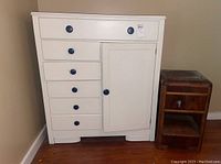 White dresser with six drawers and right-side cabinet, showing round blue knobs and general scratches.