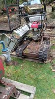 Mini tracked machine sits outdoors on grass near a fire hydrant, showing full front angled view and metal track system.