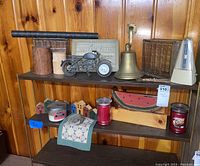 Overview of three shelves holding various home decor items including a brass bell, metal motorcycle model, candles, carved wood houses, carved watermelon, and glass block.