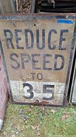 Photo of a heavily worn metal 'Reduce Speed to 35' sign with rust, holes, peeling paint, and outdoor wear.